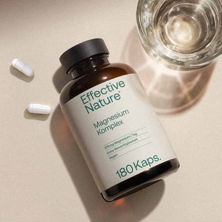 Effective Nature Magnesium Komplex, 180 Kapseln, Braunglasflasche liegend, zwei weiße Kapseln daneben, Glas Wasser