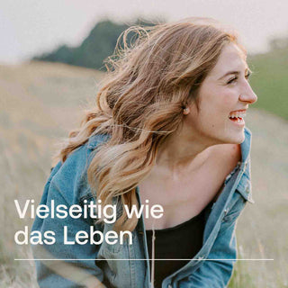 Lachende Frau mit wehenden Haaren auf einem Feld, Denim-Jacke, Text: „Vielseitig wie das Leben