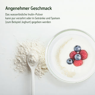 Inulin-Pulver auf einem Löffel neben einer Schüssel Joghurt mit Blaubeeren und Himbeeren, weißer Hintergrund