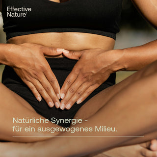 Frau in schwarzem Sport-Outfit hält Hände auf Bauch, sitzend; Text: Natürliche Synergie – für ein ausgewogenes Milieu.
