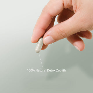 Hand hält transparente Kapsel mit grauem Pulver, Beschriftung: 100% Natural Detox Zeolith