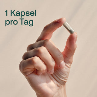 Hand hält eine transparente Kapsel mit grauem Pulver, Text: 1 Kapsel pro Tag